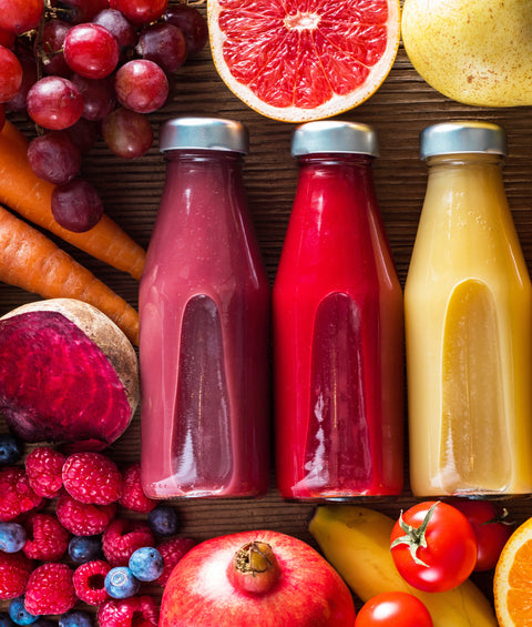 Brightly colored juice in individual bottles surrounded by fresh fruits.